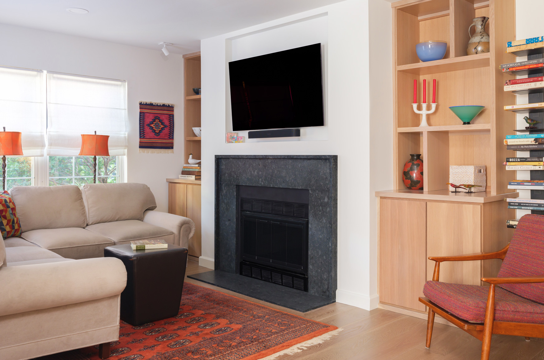 Cozy living room with modern fireplace – A warm and inviting living space by Hercules Design Build, featuring a black stone fireplace, built-in oak shelving, and a plush sectional sofa. This Central West End multi-room remodel showcases the craftsmanship of a leading design build remodeling company in St. Louis, blending comfort with refined design.