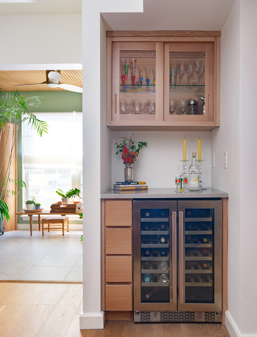 Built-in wine bar with oak cabinetry and beverage cooler – A built-in wine bar designed by Hercules Design Build features oak cabinetry, a dual-zone beverage cooler, and glass-front upper cabinets stocked with colorful stemware. Part of a multi-room remodel in the Central West End by a leading design build remodeling company in St. Louis.