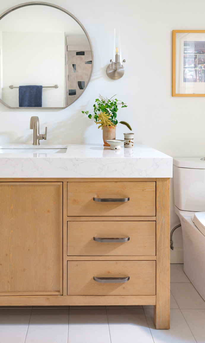 White natural bathroom with natural wood cabinets and a round mirror — Hercules Design Build in St. Louis MO Remodelers